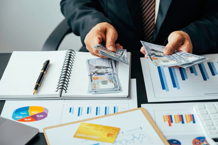A person counting cash on a table full of charts